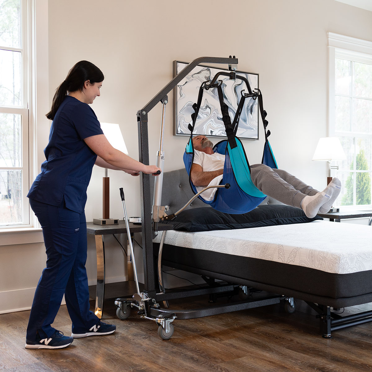 Caregiver using a Hoyer lift beside a Flexabed Hi-Low bed